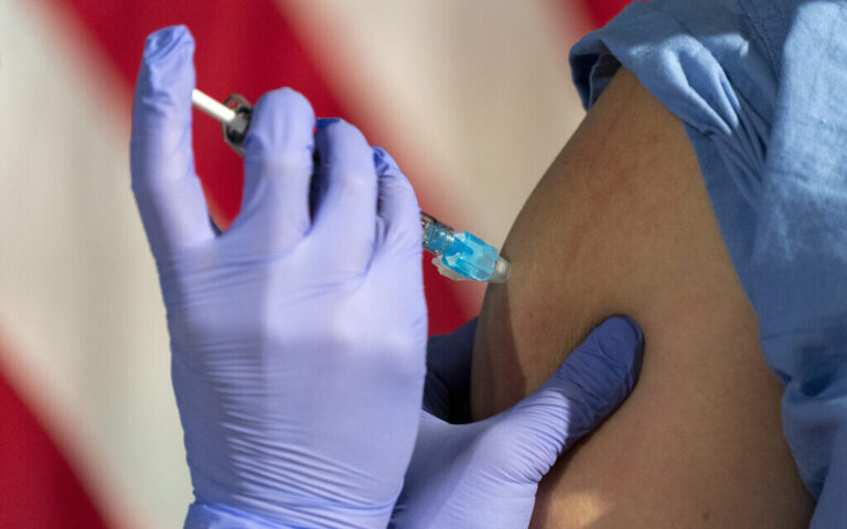 Illustrative image: In front of an American flag, nurse Lillian Wirpsza (left) administers a COVID-19 vaccine to Shylee Stewart, a labor and delivery nurse at George Washington University Hospital. (AP Photo/Jacquelyn Martin, Pool)