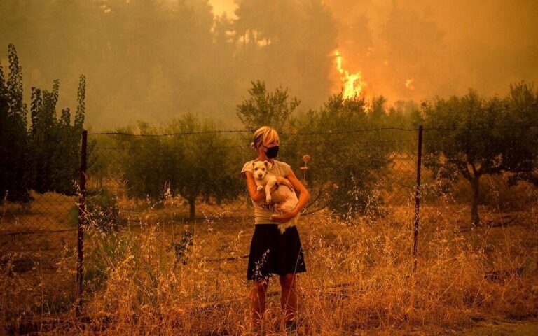 A woman holds a dog in her arms as forest fires approach the village of Pefki on Evia (Euboea) island, Greece's second largest island, on August 8, 2021 (ANGELOS TZORTZINIS / AFP)