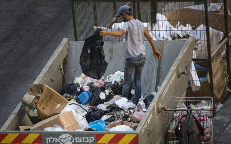 A teenager search for cans through a garbage container in the center of Jerusalem on September 02,2020. (Nati Shohat/Flash90)