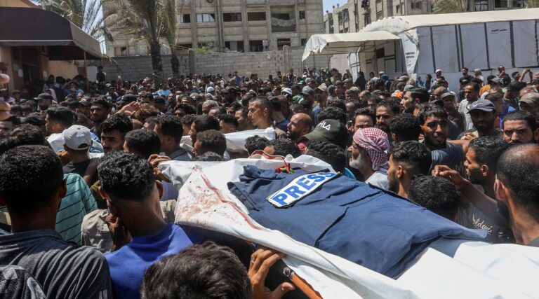 People hold up the body of a journalist killed by Israeli strikes covered in a white sheet and a press vest.