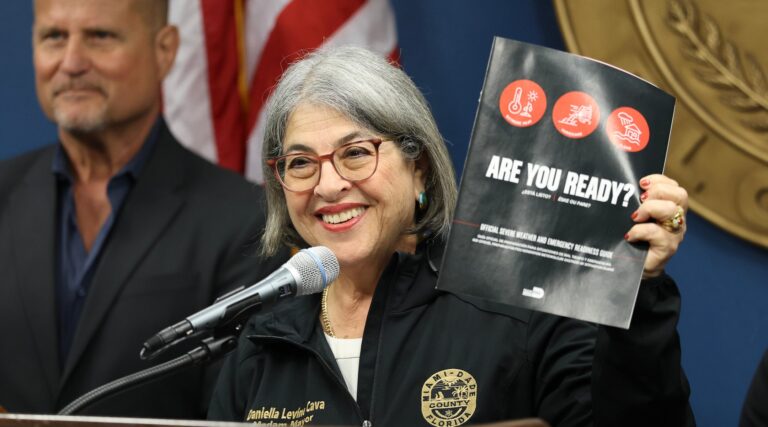 The mayor of Miami-Dade County holds an emergency preparedness book at a press conference