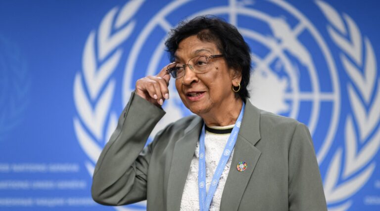 A photo of Navi Pillay adjusting her glasses in front of the UN emblem.